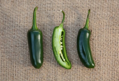 Photo of Whole and cut fresh green jalapeno peppers on sacking, flat lay