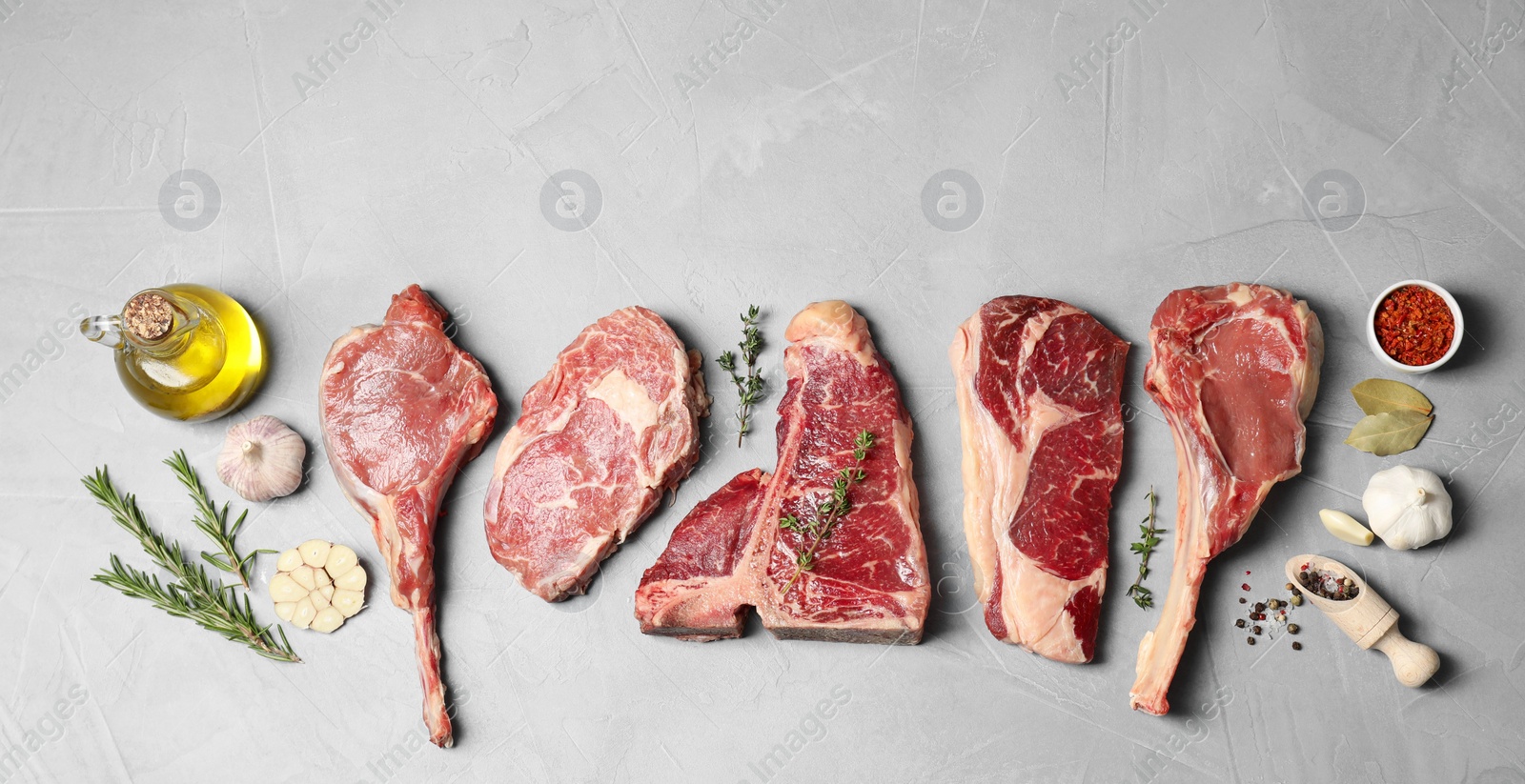 Photo of Fresh raw beef cuts, spices and oil on light grey textured table, flat lay