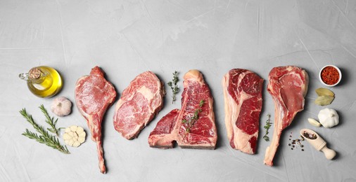 Photo of Fresh raw beef cuts, spices and oil on light grey textured table, flat lay