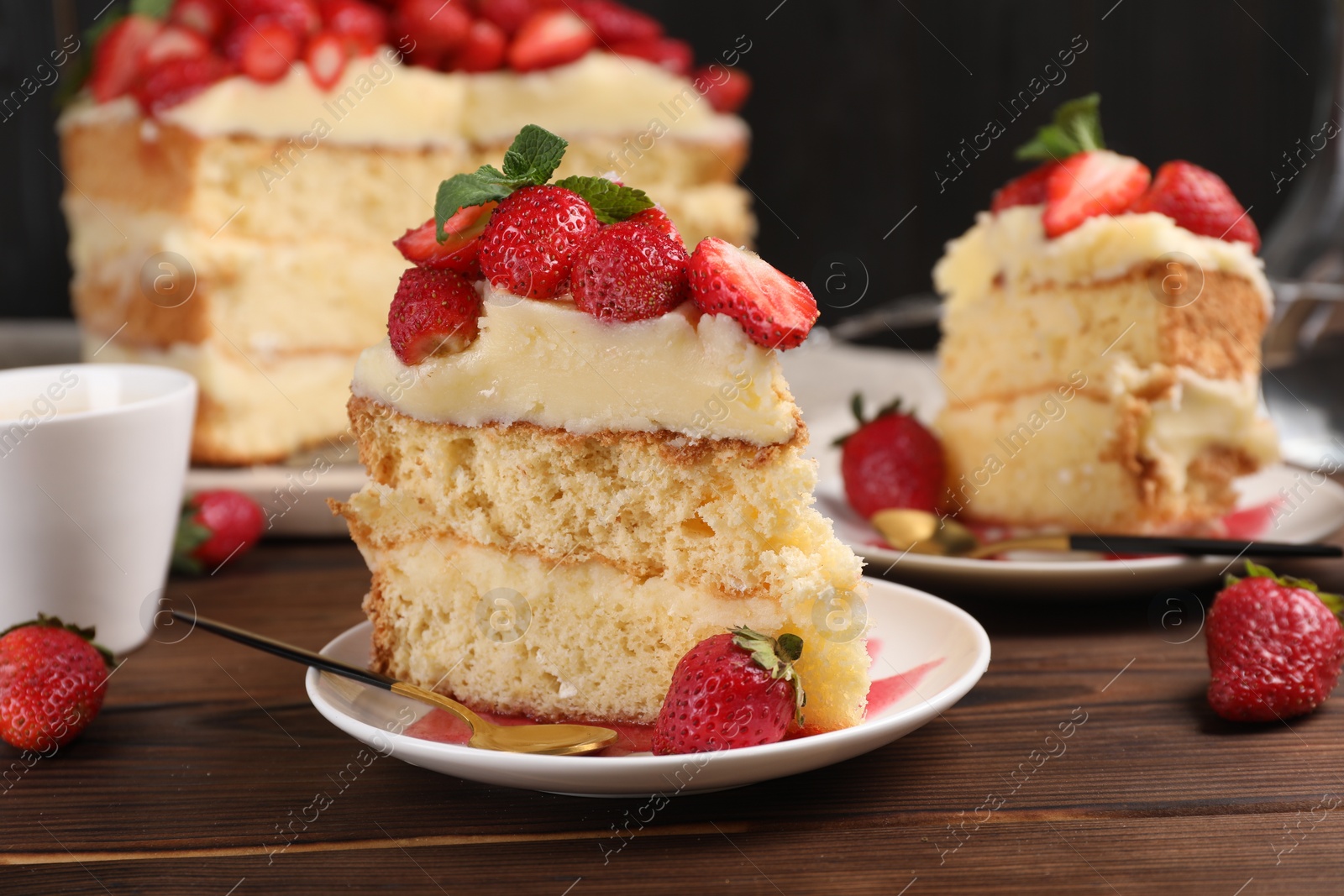 Photo of Tasty cake with fresh strawberries, mint and cup of drink on wooden table, closeup