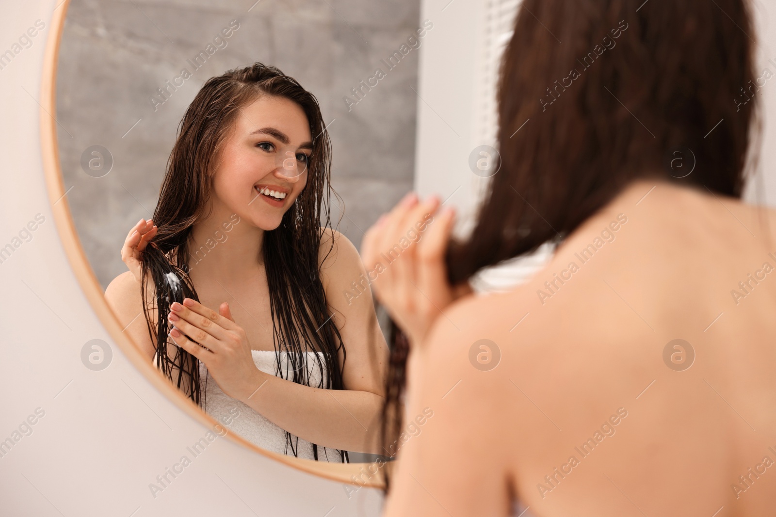 Photo of Young woman applying hair mask near mirror in bathroom