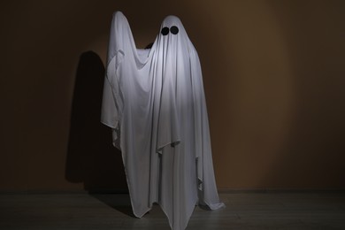 Creepy ghost. Woman covered with sheet near brown wall