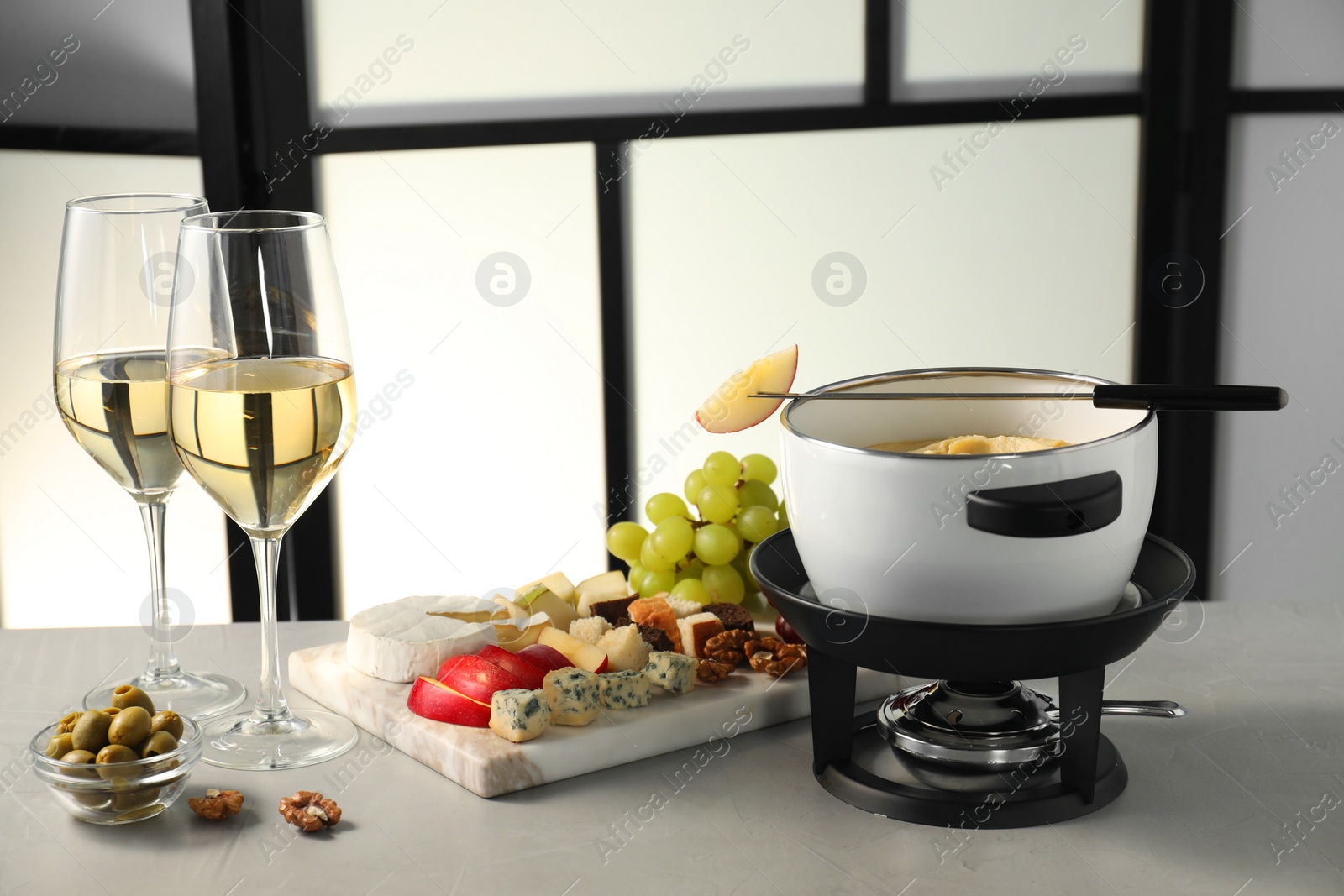 Photo of Fork with piece of apple, melted cheese in fondue pot, wine and products on grey table