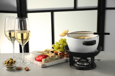 Photo of Fork with piece of apple, melted cheese in fondue pot, wine and products on grey table