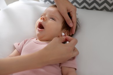 Photo of Mother cleaning ears of her baby with cotton bud on bed, closeup