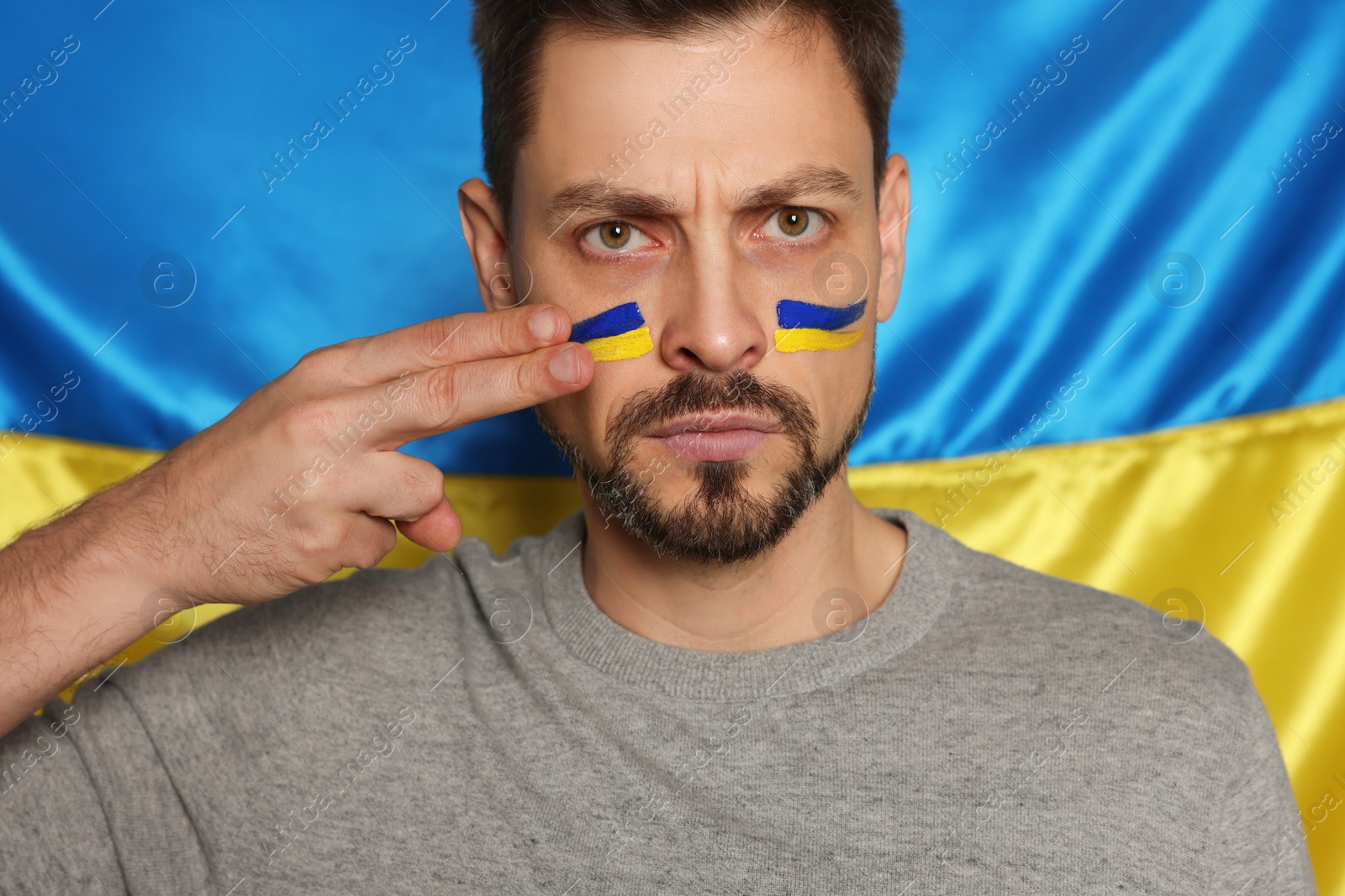 Photo of Angry man with face paint near Ukrainian flag, closeup