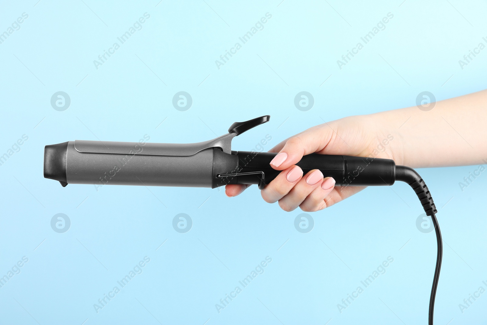 Photo of Hair styling appliance. Woman holding curling iron on light blue background, closeup