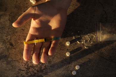 Photo of Addicted man holding syringe near drugs at grey textured table , closeup