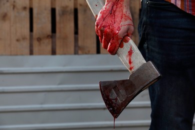 Photo of Man holding bloody axe outdoors, closeup. Space for text