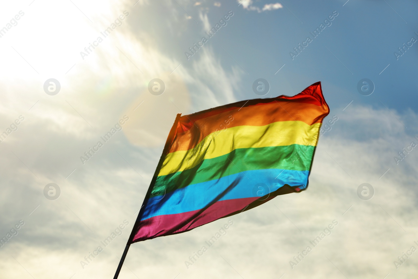 Photo of Bright LGBT flag against blue sky with clouds