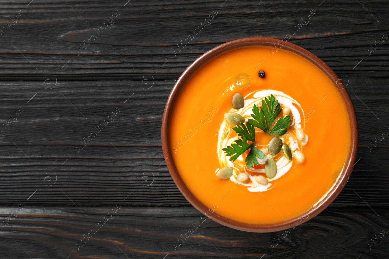 Photo of Delicious pumpkin soup in bowl on wooden table, top view. Space for text