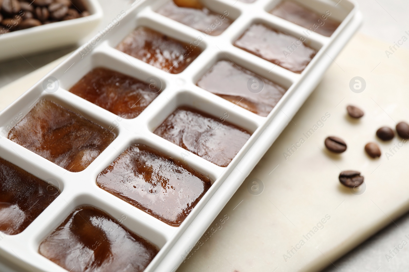 Photo of Ice cubes in tray and coffee beans on grey table, closeup