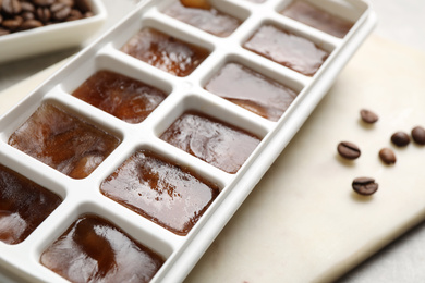 Ice cubes in tray and coffee beans on grey table, closeup