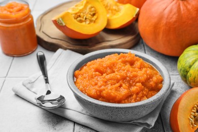 Photo of Bowl of delicious pumpkin jam and fresh pumpkin on tiled surface