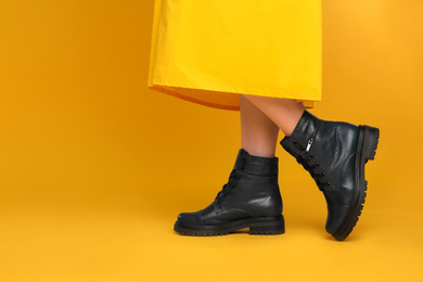 Photo of Woman wearing stylish boots on yellow background, closeup. Space for text