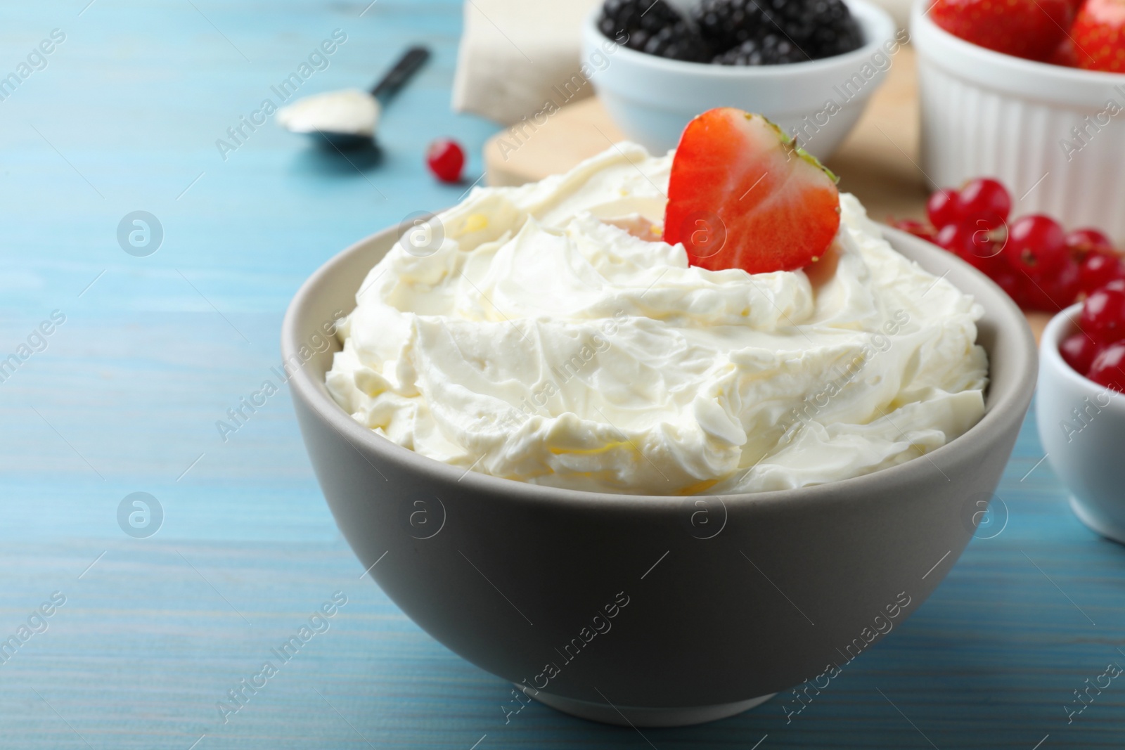 Photo of Tasty cream cheese and fresh berries on light blue wooden table