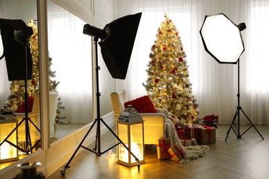 Cozy festive photo zone with armchair, Christmas tree and professional equipment indoors