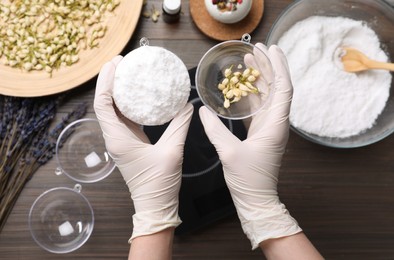 Photo of Woman in gloves making bath bomb at wooden table, top view