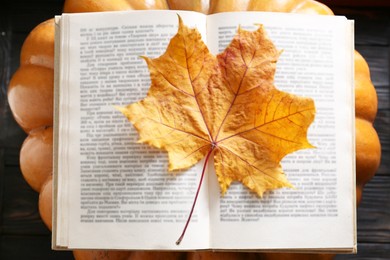 Book with autumn leaf as bookmark and ripe pumpkin on table, top view