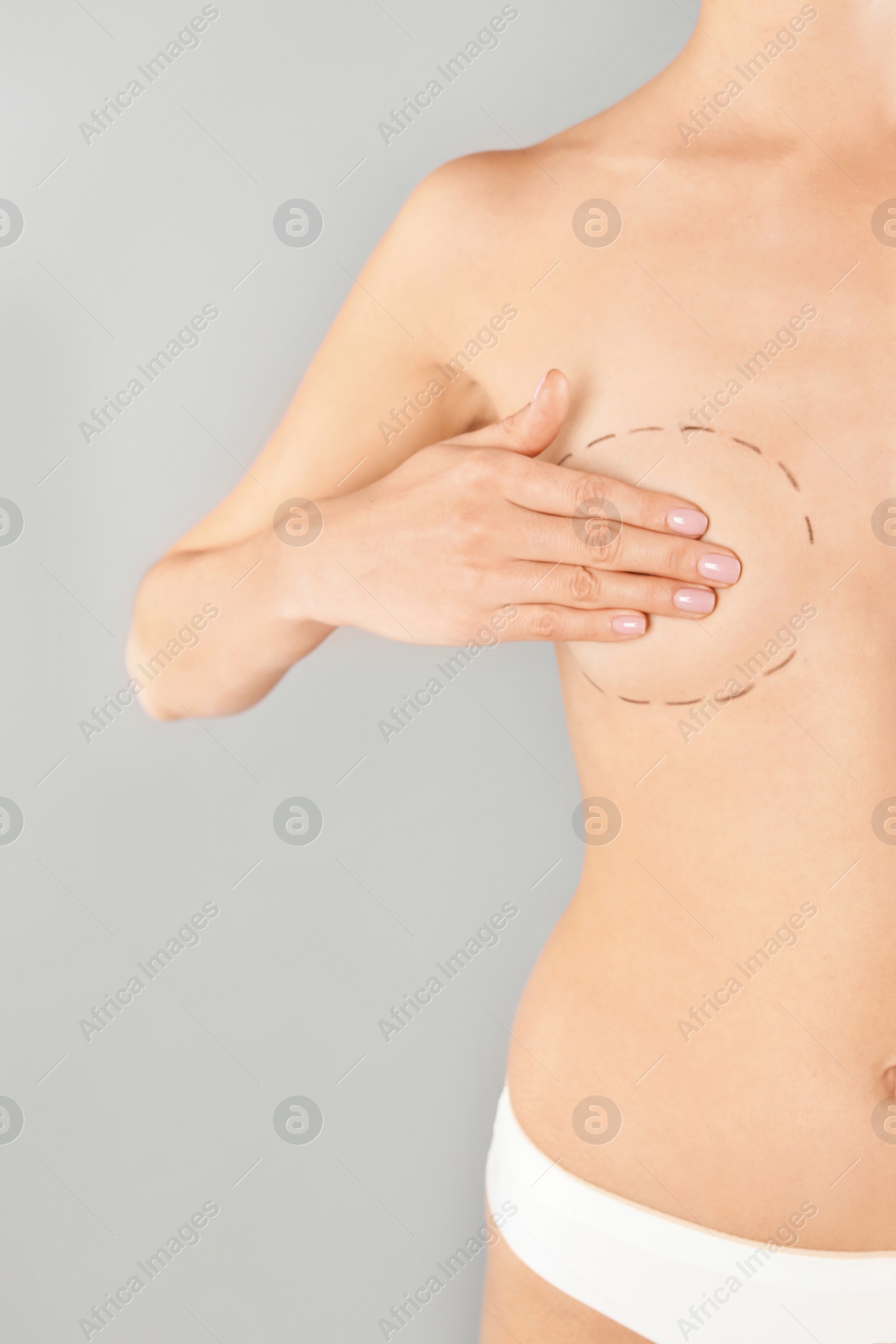 Photo of Young woman with marks on breast for cosmetic surgery operation against gray background, closeup