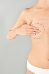 Photo of Young woman with marks on breast for cosmetic surgery operation against gray background, closeup