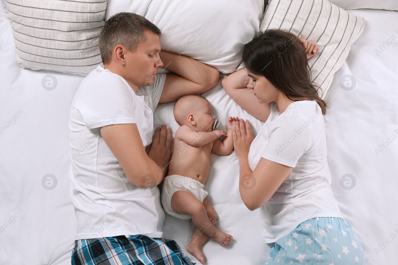 Photo of Couple and baby sleeping on bed together, top view