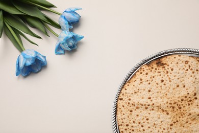Photo of Tasty matzos and fresh tulips on light grey background, flat lay. Passover (Pesach) celebration
