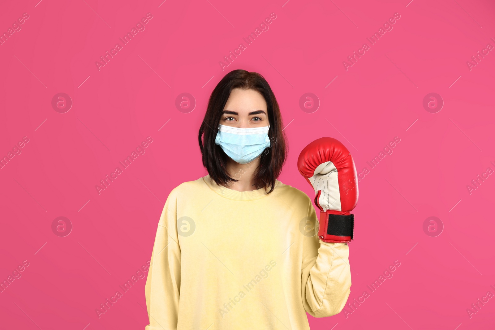 Photo of Woman with protective mask and boxing gloves on pink background. Strong immunity concept