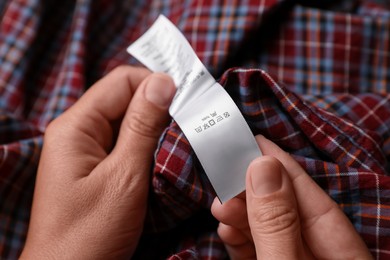 Photo of Woman holding clothing label on checkered garment, closeup