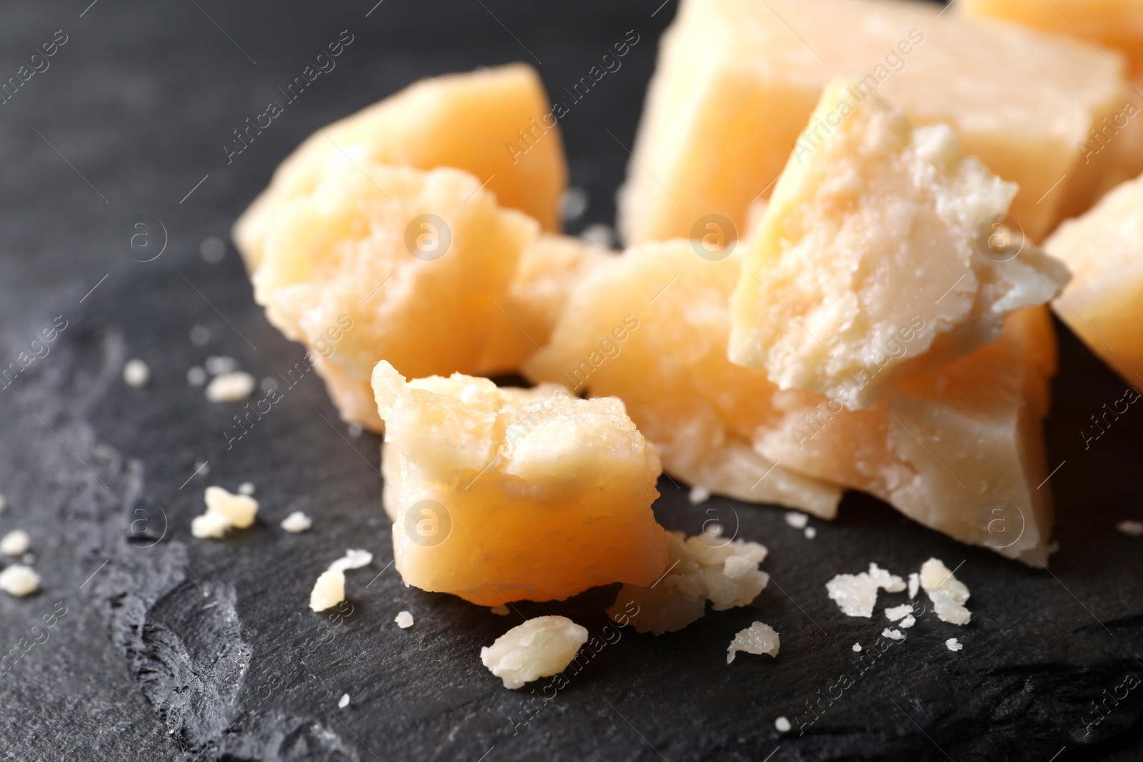 Photo of Pieces of delicious parmesan cheese on slate plate, closeup