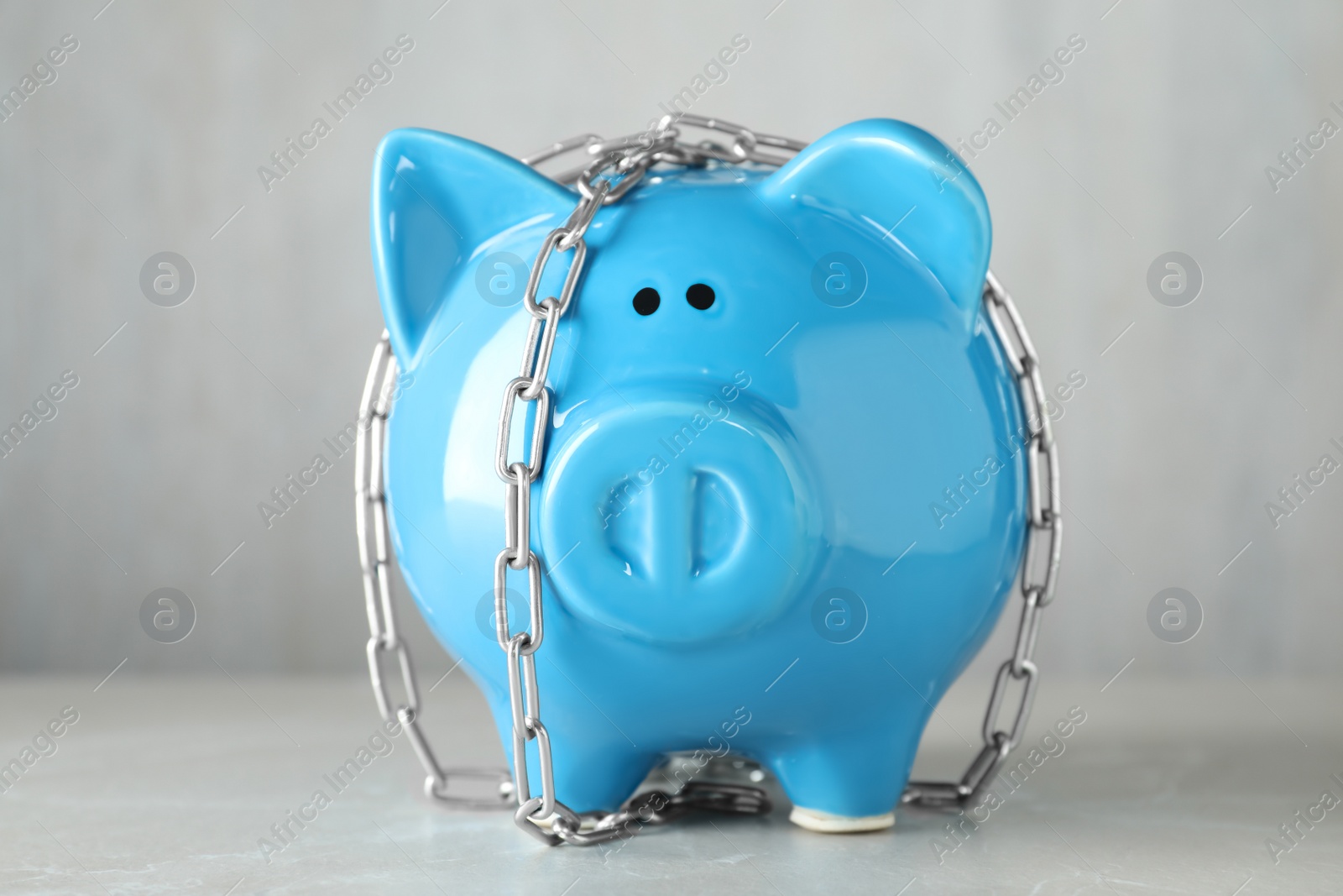 Photo of Piggy bank with steel chain on grey marble table. Money safety concept