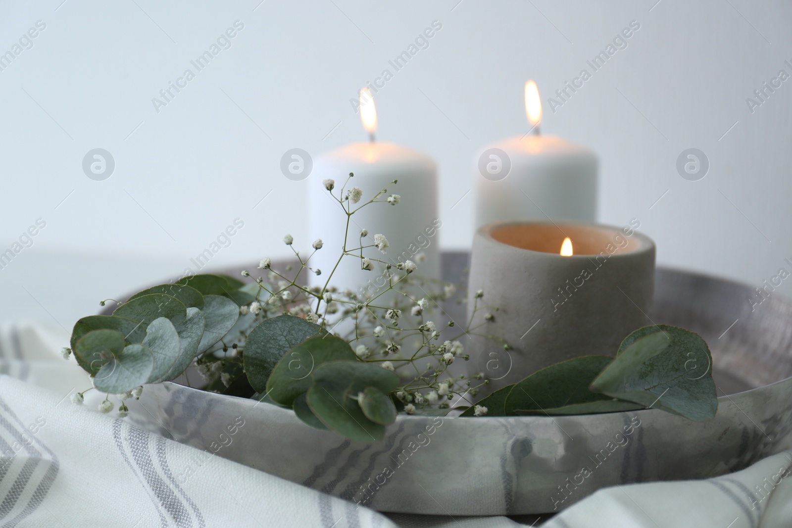 Photo of Beautiful eucalyptus branches, flowers and burning candles on fabric, closeup. Interior element