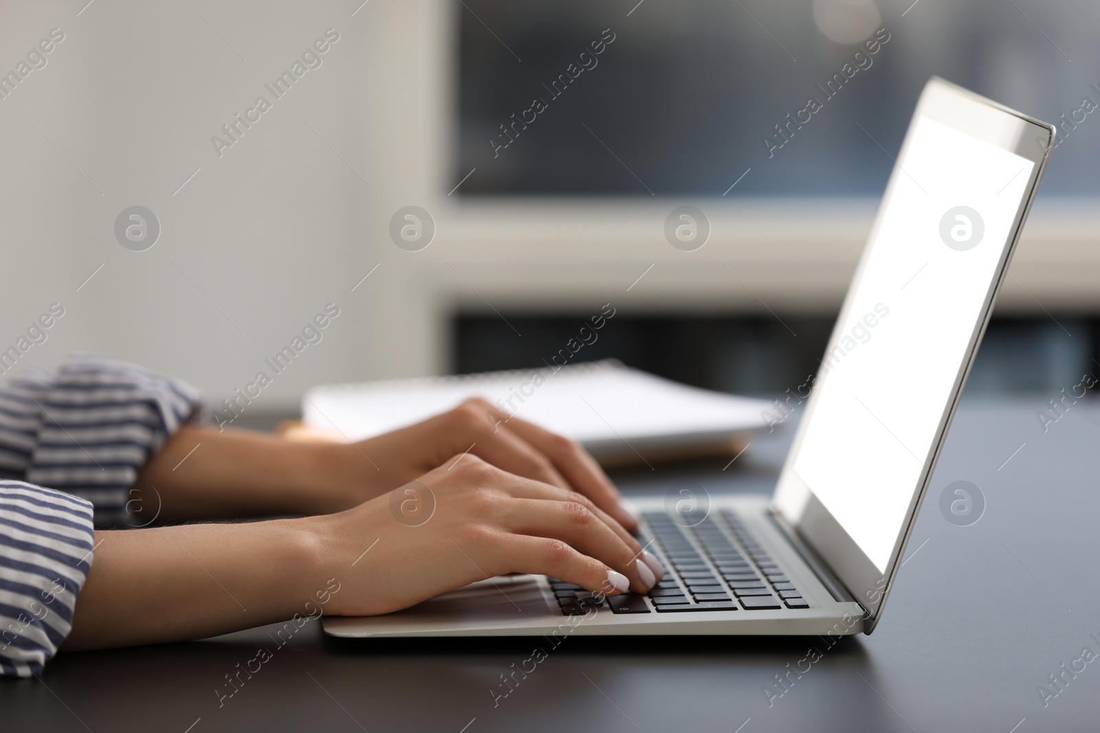 Photo of Woman using modern laptop at black desk in office, closeup