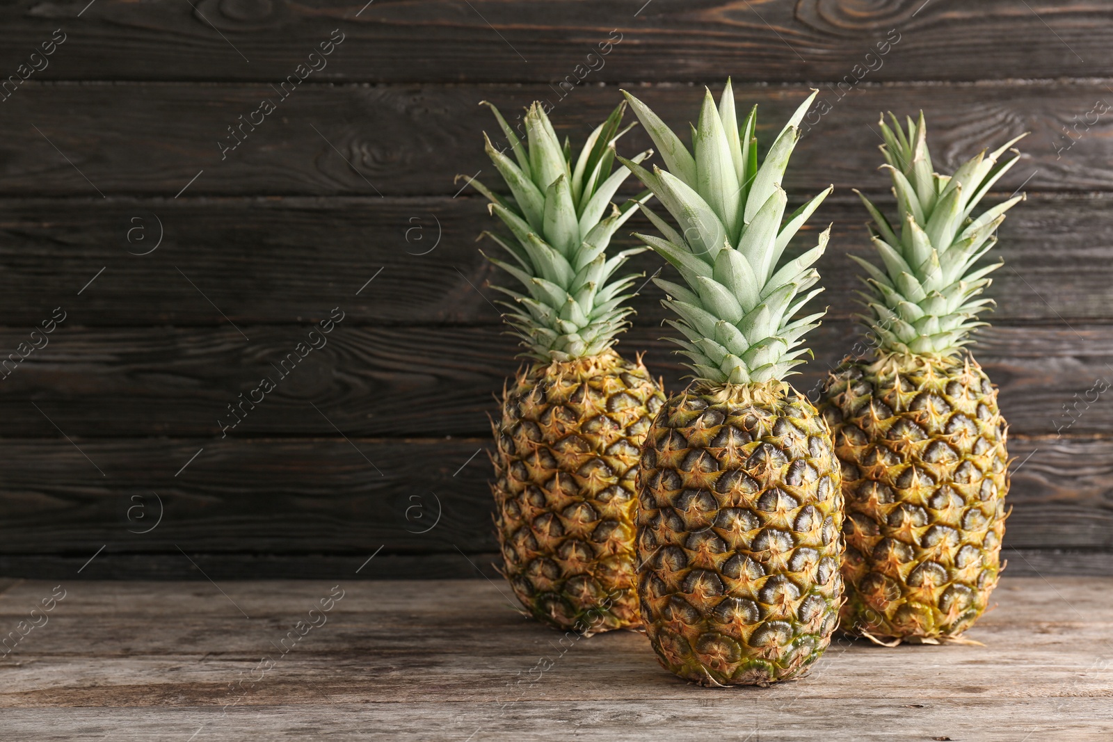 Photo of Fresh pineapples on table against wooden wall