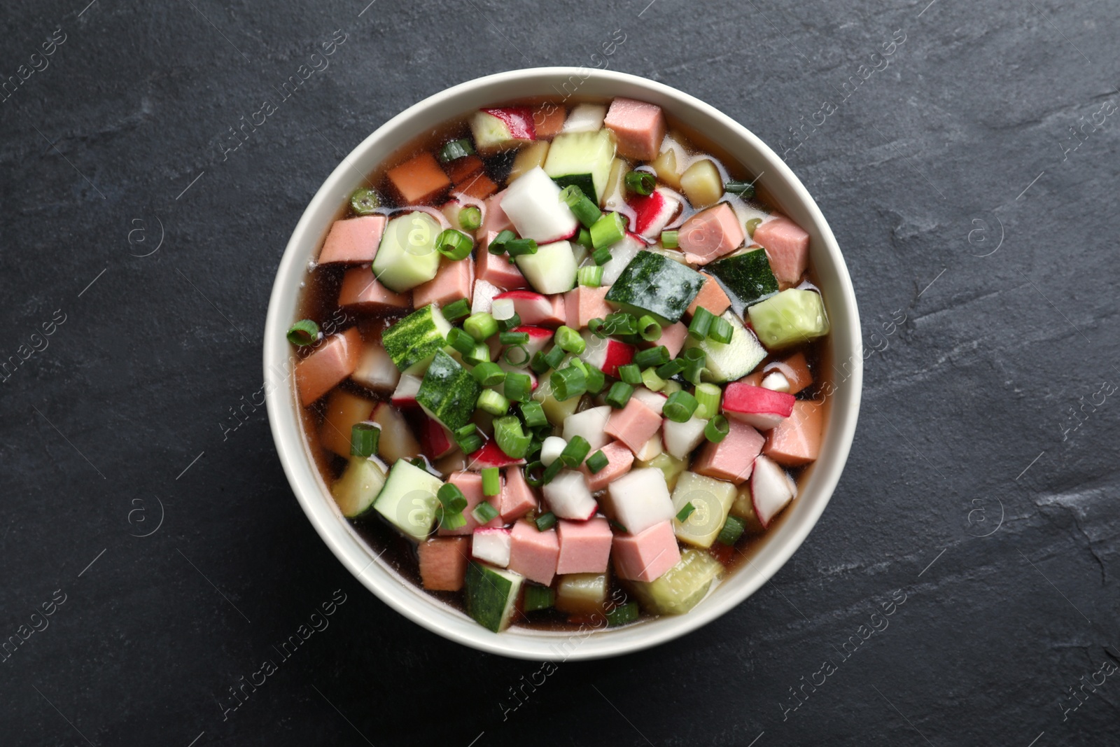 Photo of Delicious cold okroshka with kvass on black table, top view. Traditional Russian summer soup