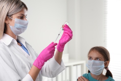 Doctor filling syringe with vaccine for little girl in hospital