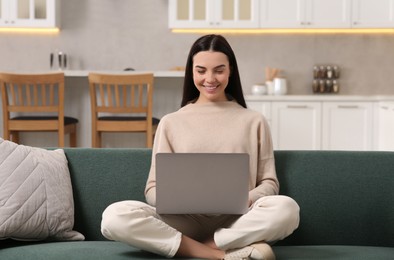 Happy woman working with laptop on sofa in kitchen