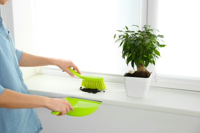 Photo of Woman sweeping away scattered soil from window sill with brush, closeup