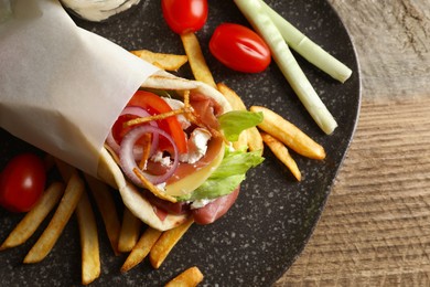 Delicious pita wrap with prosciutto, vegetables and potato fries on wooden table, top view