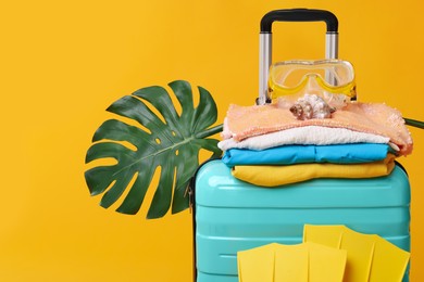 Suitcase, clothes, beach accessories and tropical leaf on yellow background. Summer vacation