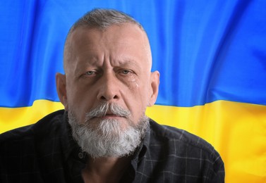Upset senior man and national flag on background. Stop war in Ukraine