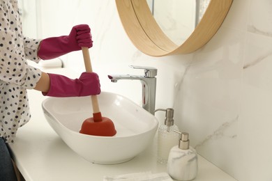 Photo of Woman using plunger to unclog sink drain in bathroom, closeup