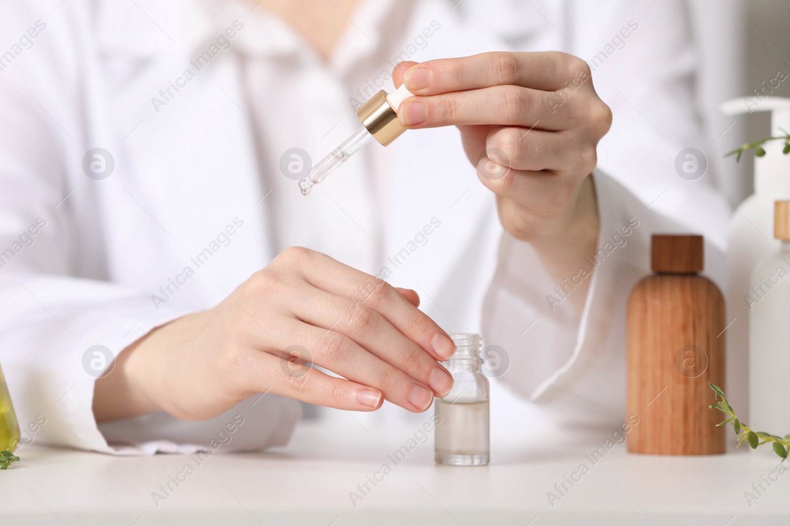 Photo of Dermatologist testing essential oil at white table indoors, selective focus