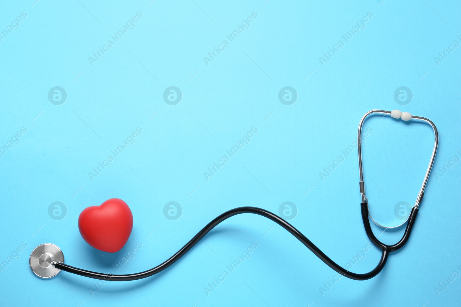 Photo of Stethoscope and red decorative heart on light blue background, flat lay with space for text. Cardiology concept