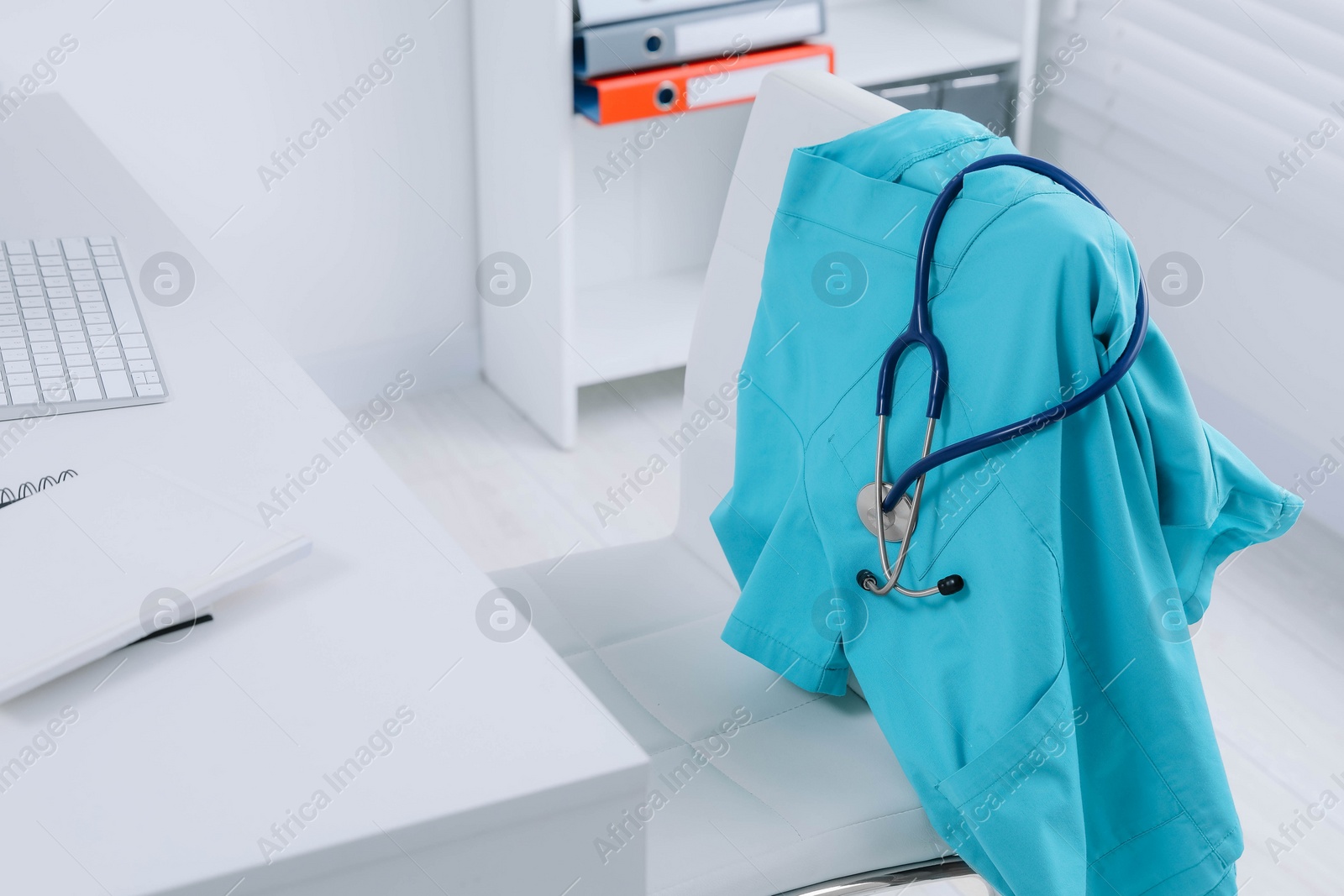 Photo of Turquoise medical uniform and stethoscope hanging on chair in clinic