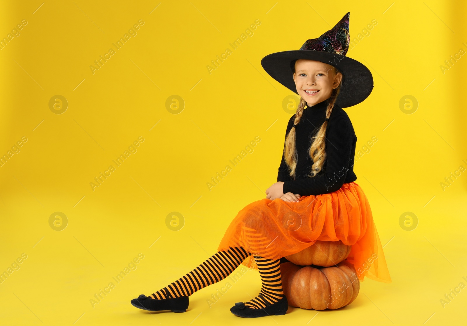 Photo of Cute little girl with pumpkins wearing Halloween costume on yellow background. Space for text