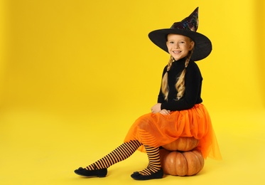 Cute little girl with pumpkins wearing Halloween costume on yellow background. Space for text