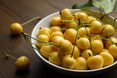 Bowl with ripe yellow cherries on wooden table, closeup