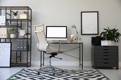 Photo of Comfortable office chair near desk with modern computer indoors