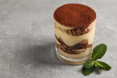 Photo of Delicious tiramisu in glass and mint on grey textured table, closeup. Space for text